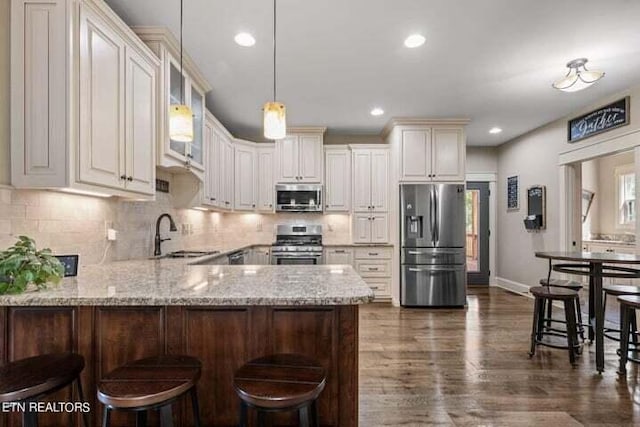 kitchen featuring stainless steel appliances, light stone countertops, kitchen peninsula, sink, and decorative light fixtures