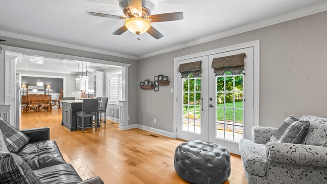 living room with a healthy amount of sunlight, french doors, crown molding, and light hardwood / wood-style flooring