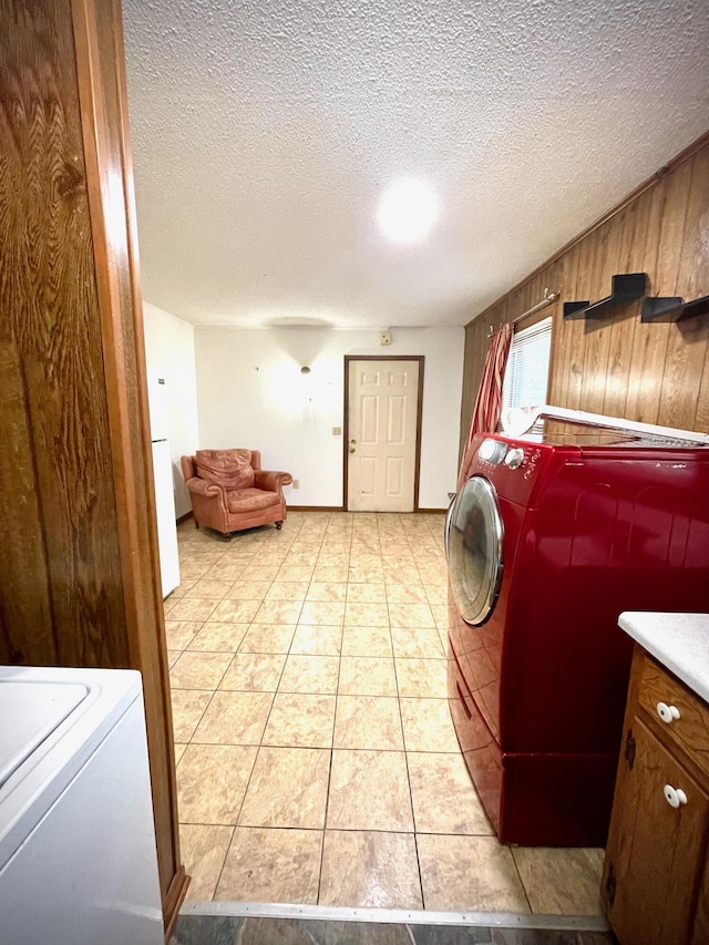 laundry room featuring washer and dryer, a textured ceiling, wood walls, and light tile patterned flooring