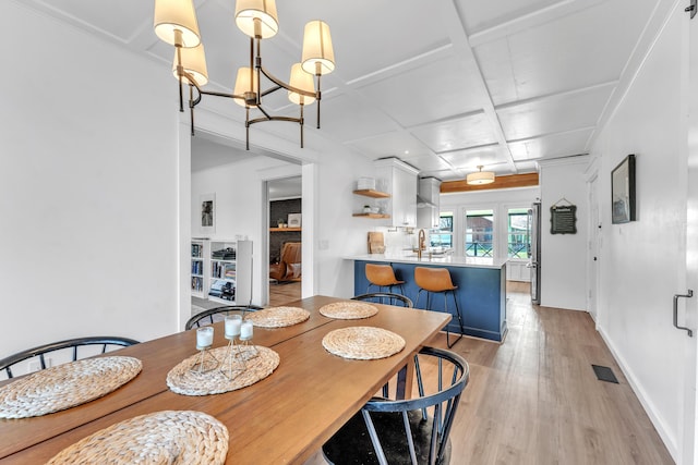 dining room featuring light wood-type flooring, visible vents, a notable chandelier, coffered ceiling, and baseboards