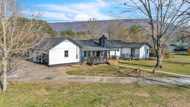 view of front of property with a deck, dirt driveway, board and batten siding, a front yard, and a chimney