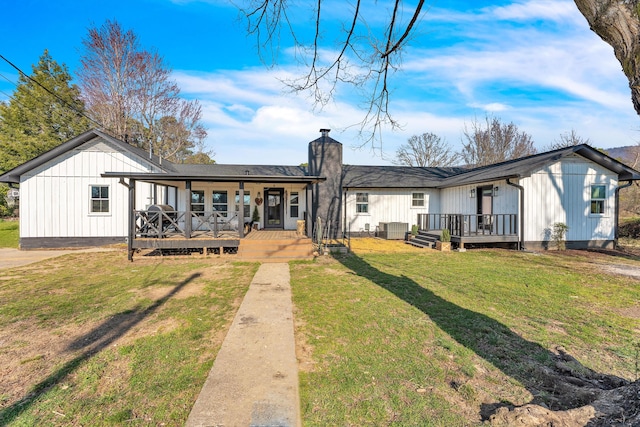 back of property with a lawn, board and batten siding, a deck, and a chimney