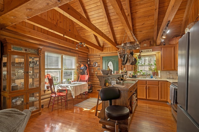 kitchen with light hardwood / wood-style floors, beamed ceiling, appliances with stainless steel finishes, log walls, and wooden ceiling