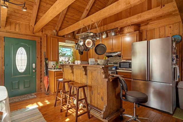 kitchen with appliances with stainless steel finishes, wood ceiling, rail lighting, a kitchen breakfast bar, and hardwood / wood-style flooring