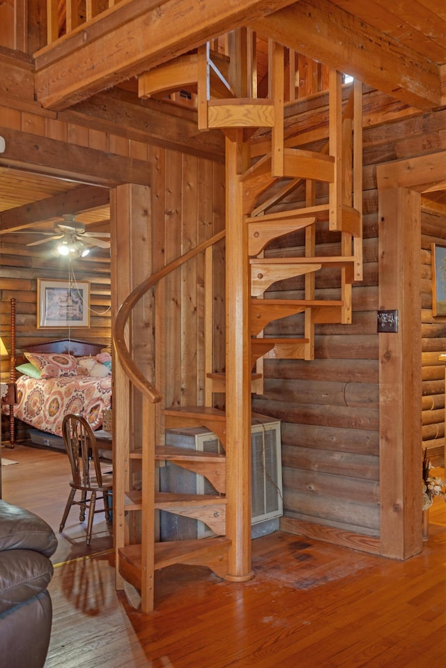 stairway with ceiling fan, hardwood / wood-style floors, rustic walls, and beam ceiling