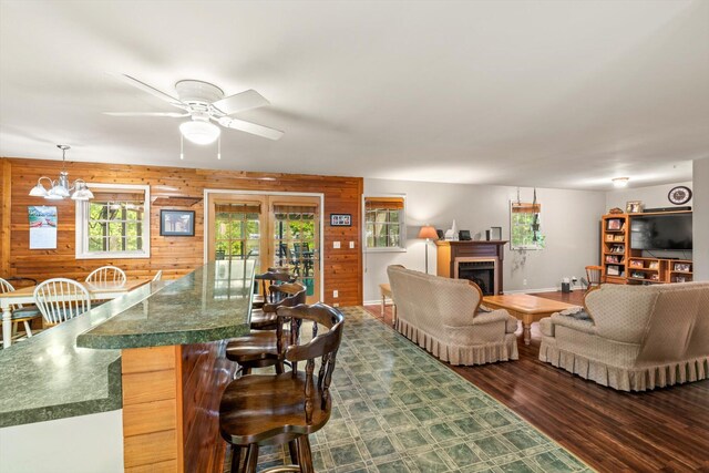 living room featuring ceiling fan with notable chandelier, wood walls, and dark hardwood / wood-style flooring