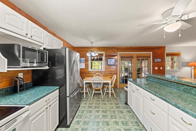 kitchen featuring white cabinetry, french doors, ceiling fan, hanging light fixtures, and wooden walls