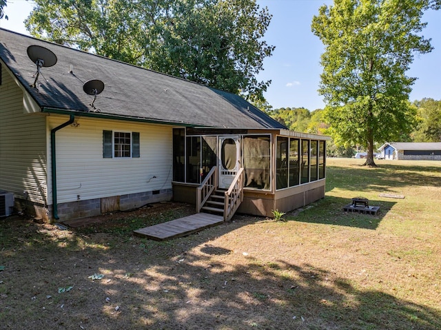 back of house featuring a lawn, a sunroom, and an outdoor fire pit