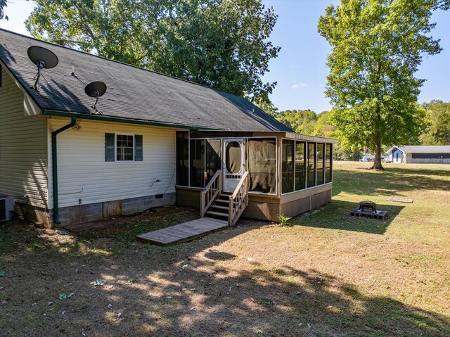 back of house featuring a lawn, a sunroom, and an outdoor fire pit