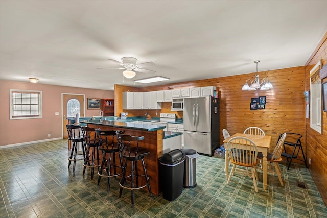 kitchen with pendant lighting, a breakfast bar area, wooden walls, white cabinets, and appliances with stainless steel finishes