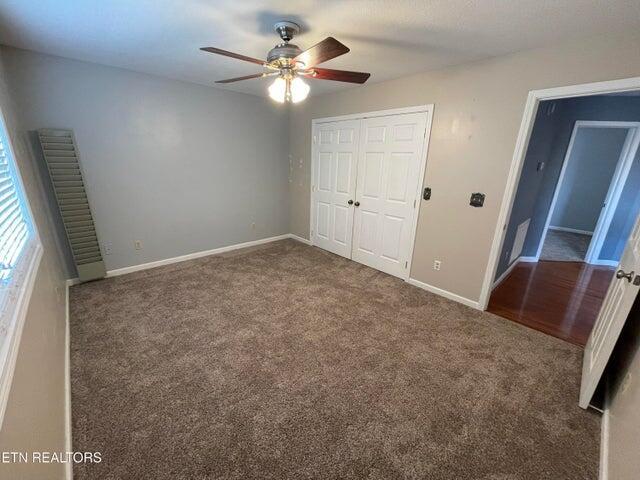 unfurnished bedroom with ceiling fan, a closet, and dark colored carpet