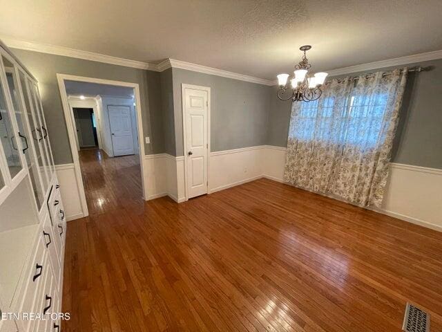 unfurnished dining area with dark hardwood / wood-style flooring, crown molding, a textured ceiling, and an inviting chandelier