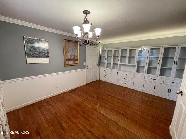 unfurnished dining area with ornamental molding, dark hardwood / wood-style floors, and an inviting chandelier