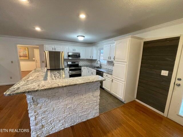 kitchen with sink, backsplash, stainless steel appliances, light stone countertops, and white cabinets