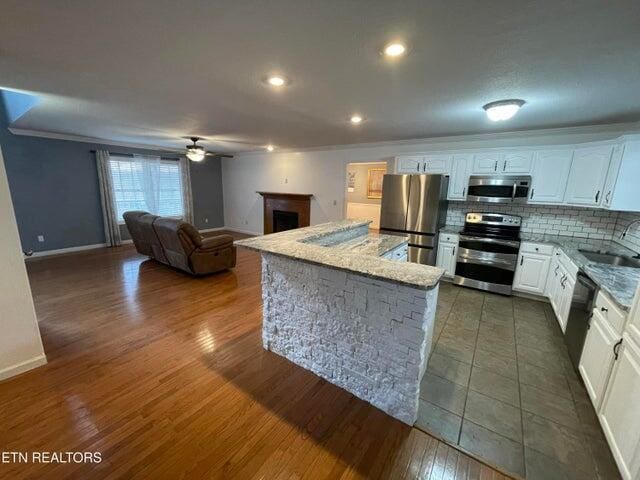 kitchen featuring a kitchen island, tasteful backsplash, white cabinets, ceiling fan, and stainless steel appliances