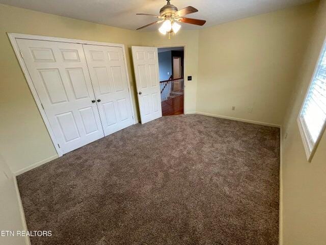 unfurnished bedroom featuring dark carpet, a closet, and ceiling fan