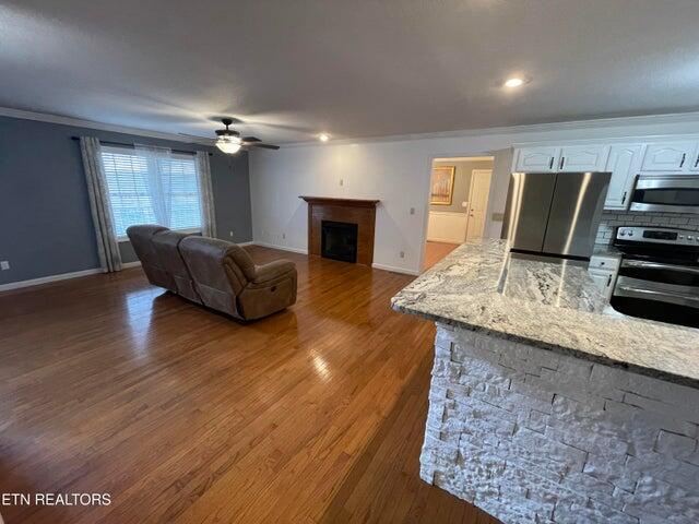 living room featuring ornamental molding, a stone fireplace, ceiling fan, and dark hardwood / wood-style flooring