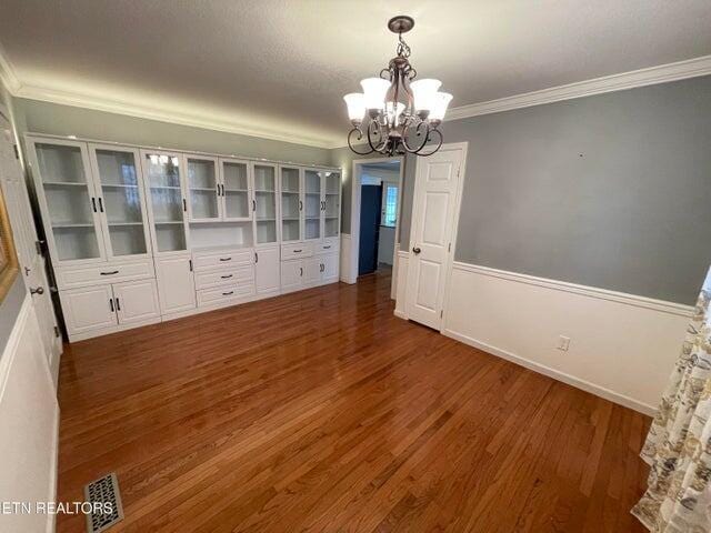 unfurnished dining area featuring ornamental molding, dark hardwood / wood-style flooring, and an inviting chandelier