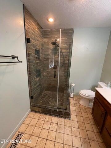 bathroom with vanity, a textured ceiling, tile patterned floors, toilet, and walk in shower