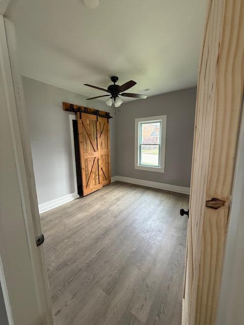 1220 Hardwick St SE, Cleveland, TN 37311 - unfurnished bedroom featuring baseboards, a barn door, light wood-style floors, and a ceiling fan