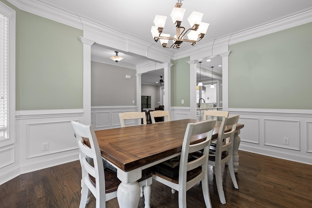 dining space featuring decorative columns, dark hardwood / wood-style flooring, ceiling fan with notable chandelier, and ornamental molding