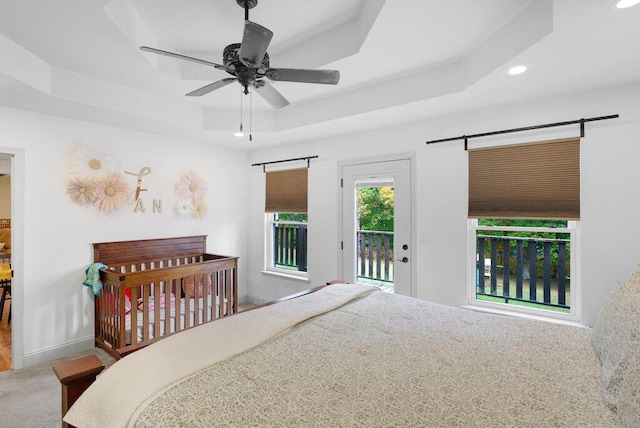 bedroom with ceiling fan, access to exterior, carpet floors, and a tray ceiling