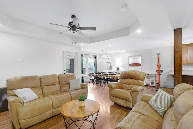 living room featuring a tray ceiling, ceiling fan, and light wood-type flooring