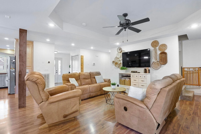 living room with ceiling fan, light wood-type flooring, and a tray ceiling