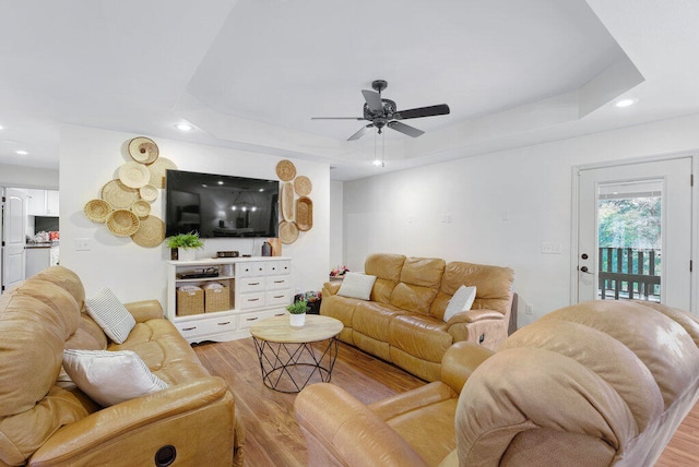 living room featuring a tray ceiling, ceiling fan, and light hardwood / wood-style flooring