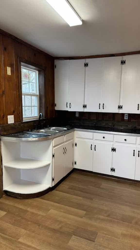 kitchen with white cabinets, wooden walls, and light hardwood / wood-style flooring