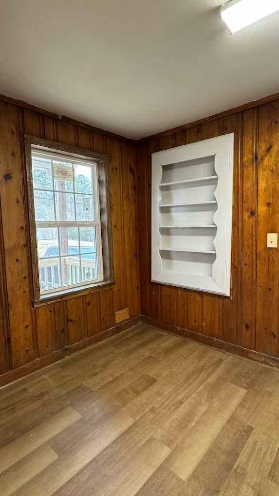 empty room featuring built in shelves, wooden walls, and light wood-type flooring