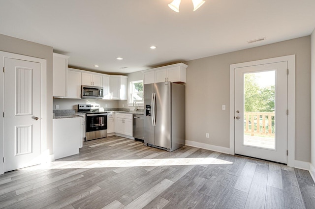 kitchen featuring light stone countertops, light hardwood / wood-style flooring, white cabinets, and appliances with stainless steel finishes