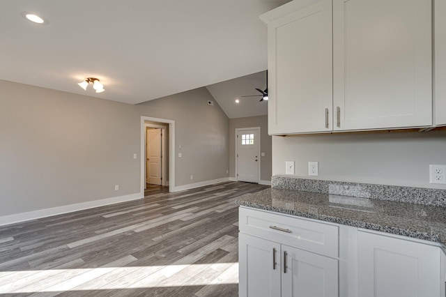 kitchen with white cabinets, light hardwood / wood-style floors, dark stone counters, and vaulted ceiling