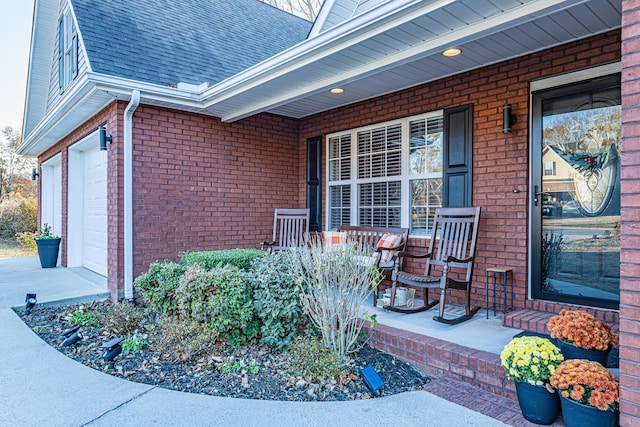 property entrance with brick siding, a porch, concrete driveway, and roof with shingles