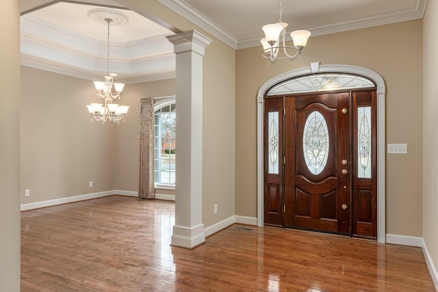 foyer featuring hardwood / wood-style floors, decorative columns, an inviting chandelier, and crown molding