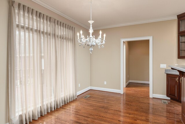 unfurnished dining area featuring hardwood / wood-style flooring, an inviting chandelier, and crown molding