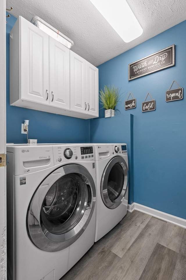 clothes washing area featuring hardwood / wood-style flooring, a textured ceiling, cabinets, and washing machine and clothes dryer