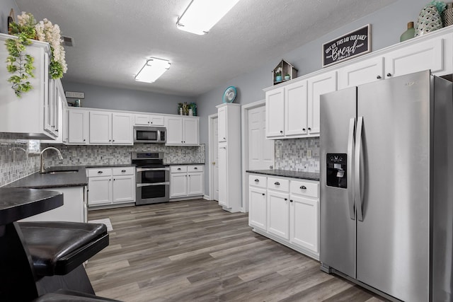 kitchen with dark wood-type flooring, sink, appliances with stainless steel finishes, white cabinets, and backsplash