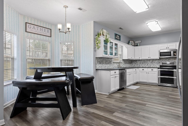 kitchen with decorative light fixtures, white cabinets, hardwood / wood-style flooring, stainless steel appliances, and a textured ceiling