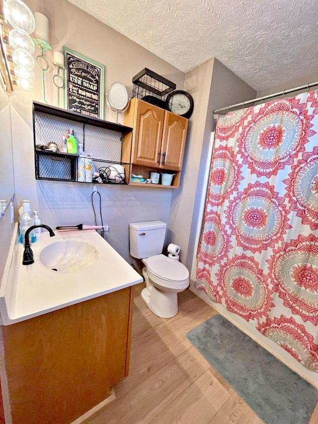 bathroom featuring walk in shower, vanity, a textured ceiling, hardwood / wood-style flooring, and toilet