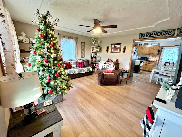 living room featuring ceiling fan, light hardwood / wood-style flooring, and a textured ceiling