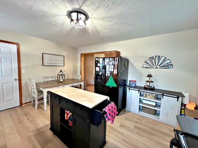 kitchen with a textured ceiling, light wood-type flooring, black fridge, and butcher block counters