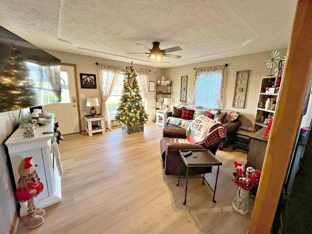 living room featuring ceiling fan, light hardwood / wood-style flooring, and a textured ceiling