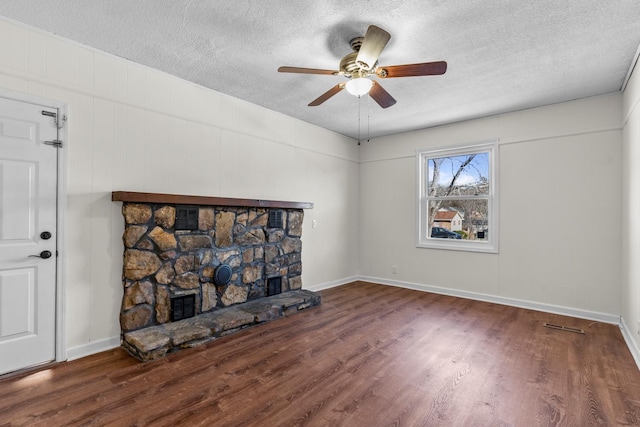 living room with ceiling fan, dark wood-type flooring, a stone fireplace, and a textured ceiling