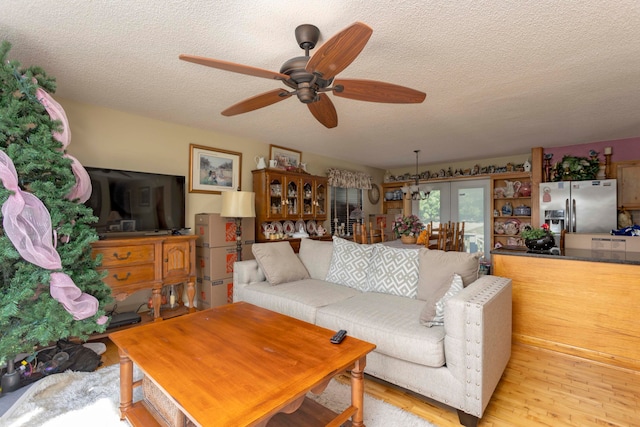 living room featuring ceiling fan, light wood-type flooring, and a textured ceiling