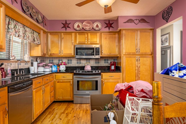 kitchen with sink, decorative backsplash, light wood-type flooring, a textured ceiling, and stainless steel appliances