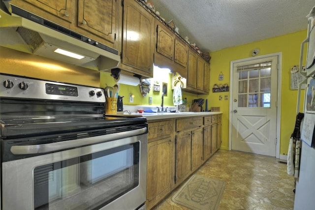 kitchen featuring stainless steel range with electric stovetop, under cabinet range hood, a textured ceiling, a sink, and brown cabinets