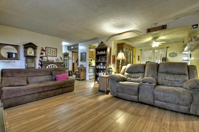 living room with light wood-type flooring, ceiling fan, and a textured ceiling