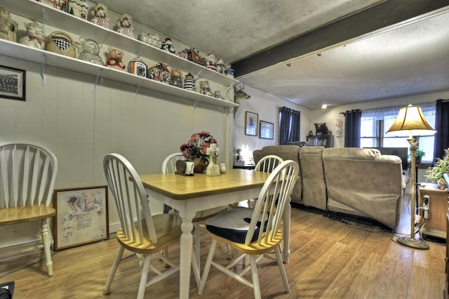 dining space with a textured ceiling, light wood-style floors, and beamed ceiling