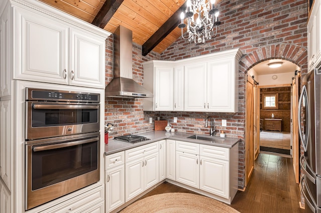 kitchen with stainless steel appliances, sink, wall chimney range hood, wooden ceiling, and white cabinetry